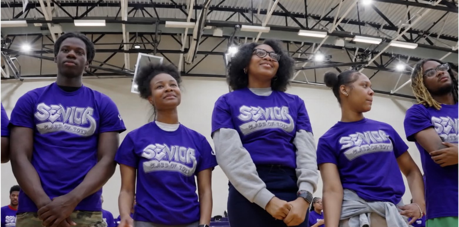 Seniors in purple Class shirts stand together in a school gym, smiling.