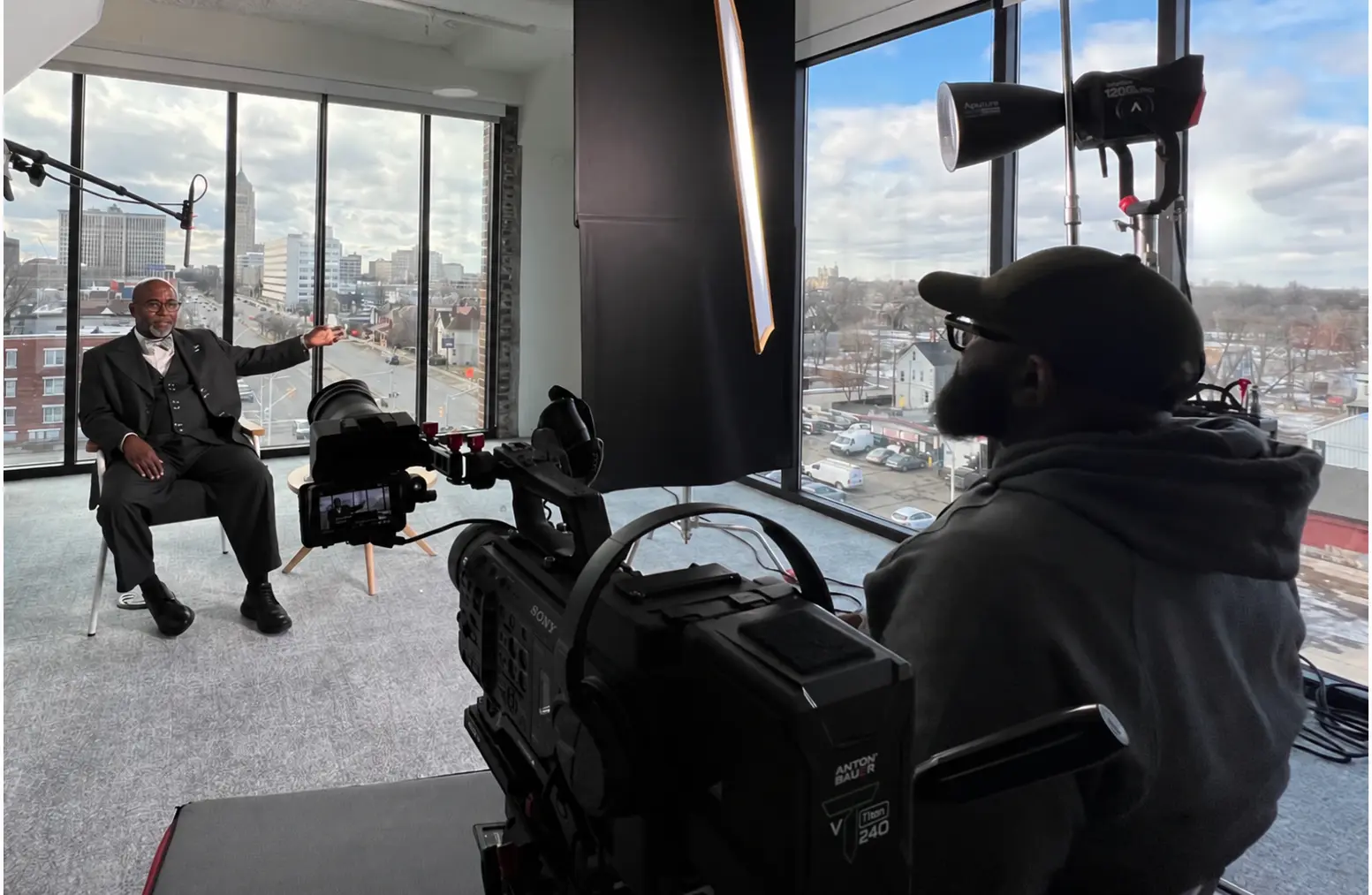 A film crew records an interview in a high-rise studio overlooking Detroit.